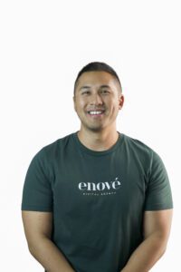 A smiling man wearing a dark green t-shirt with "enov&eacute; DIGITAL AGENCY" printed on the front.