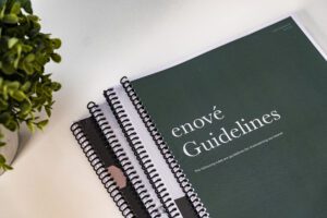 enov&eacute; Guidelines booklet with spiral binding on a white surface next to a green plant