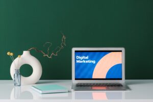 Laptop displaying 'Digital Marketing' text on screen with notebook and decorative vase on desk